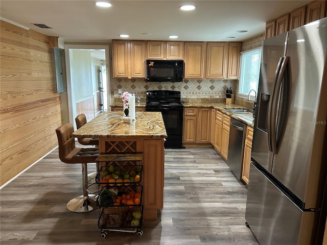 kitchen with wood walls, sink, black appliances, light stone countertops, and wood-type flooring