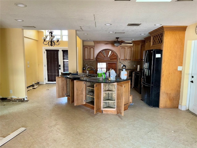 kitchen featuring an island with sink, black refrigerator, plenty of natural light, and ceiling fan with notable chandelier