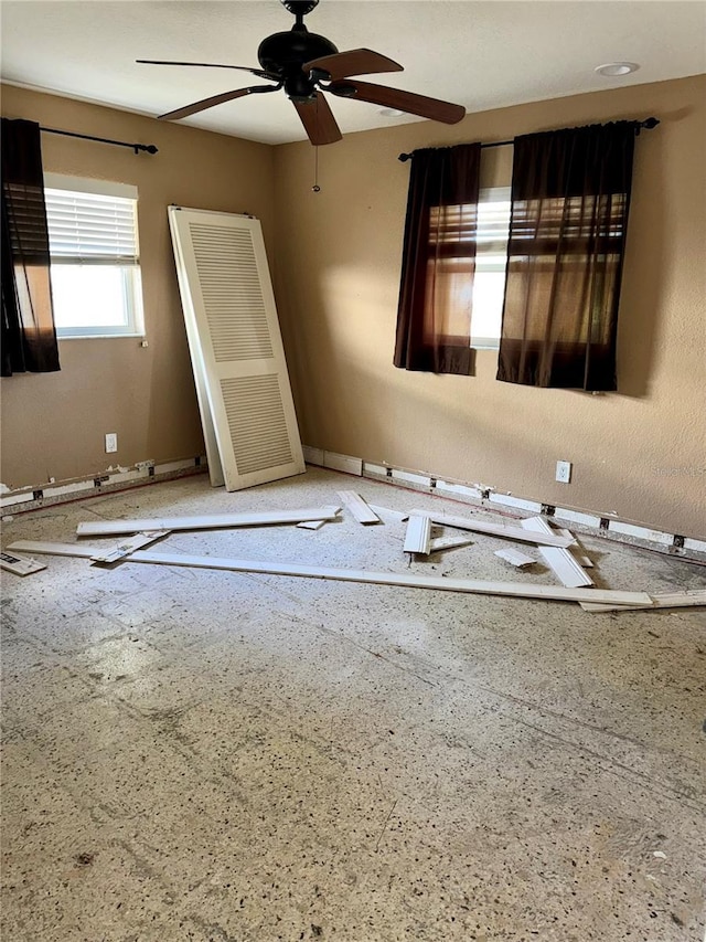 unfurnished room featuring baseboards, speckled floor, and ceiling fan