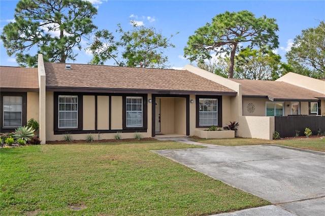 ranch-style home featuring roof with shingles, fence, a front lawn, and stucco siding