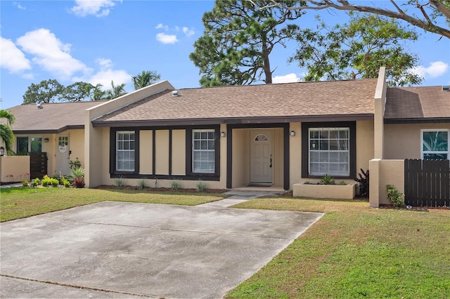 ranch-style home featuring roof with shingles, a front yard, fence, and stucco siding