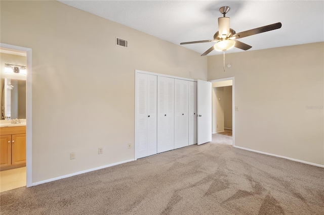 unfurnished bedroom featuring a closet, light carpet, ceiling fan, and ensuite bath