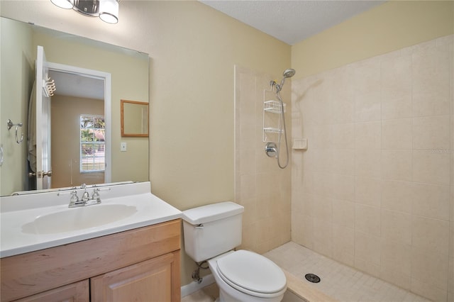 bathroom featuring toilet, vanity, a textured ceiling, and a tile shower