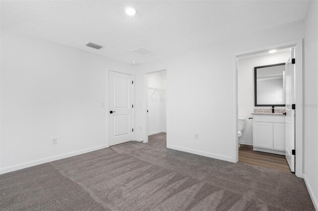 unfurnished bedroom featuring dark colored carpet, a textured ceiling, ensuite bathroom, a closet, and a spacious closet