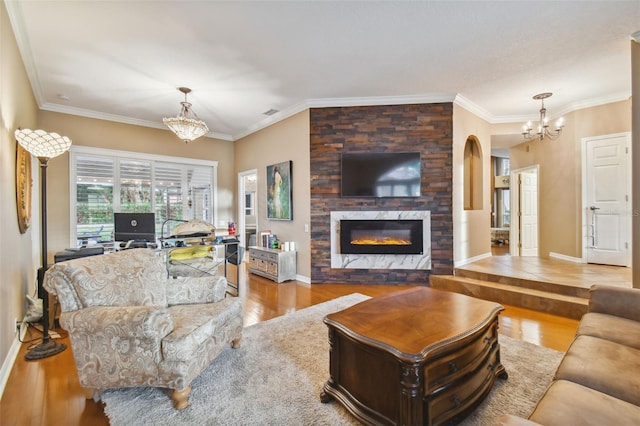 living room featuring a large fireplace, an inviting chandelier, light wood-type flooring, and crown molding