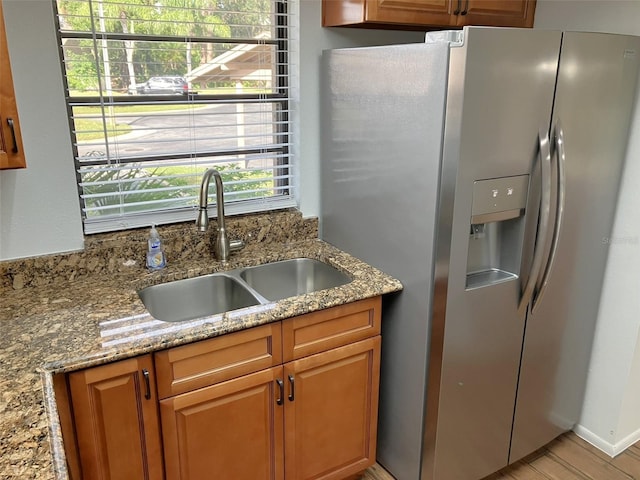 kitchen featuring light stone counters, stainless steel fridge with ice dispenser, and sink