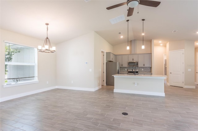 kitchen with a center island with sink, appliances with stainless steel finishes, decorative light fixtures, light hardwood / wood-style flooring, and vaulted ceiling