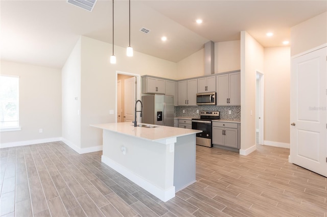 kitchen featuring gray cabinets, stainless steel appliances, light wood-type flooring, and an island with sink