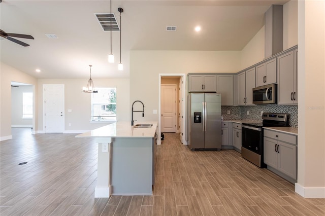 kitchen with light hardwood / wood-style floors, sink, appliances with stainless steel finishes, hanging light fixtures, and an island with sink