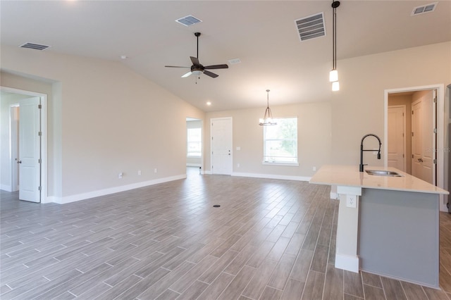 kitchen featuring wood-type flooring, decorative light fixtures, sink, an island with sink, and lofted ceiling