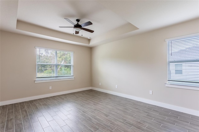 spare room with light wood-type flooring, a wealth of natural light, and a tray ceiling