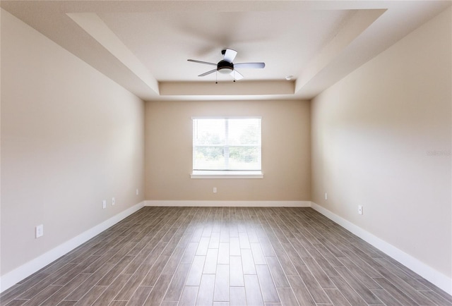 empty room featuring dark wood-type flooring, ceiling fan, and a raised ceiling