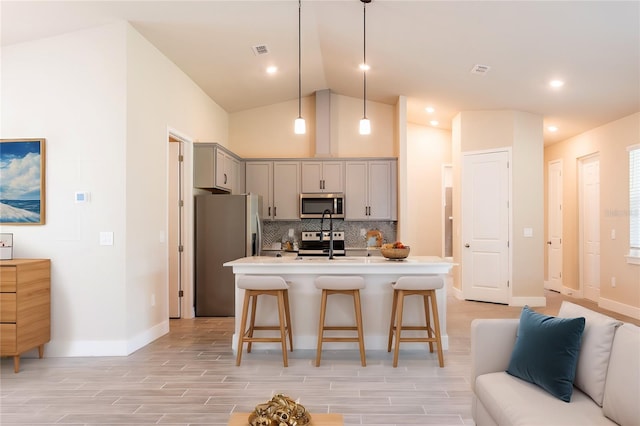 kitchen with stainless steel appliances, an island with sink, gray cabinetry, backsplash, and decorative light fixtures