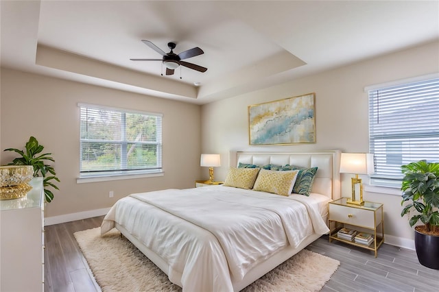 bedroom with hardwood / wood-style flooring, multiple windows, ceiling fan, and a tray ceiling