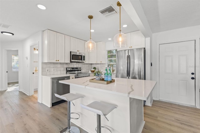 kitchen featuring light hardwood / wood-style flooring, pendant lighting, appliances with stainless steel finishes, and white cabinets