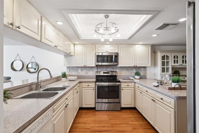 kitchen featuring appliances with stainless steel finishes, a raised ceiling, sink, pendant lighting, and light hardwood / wood-style floors