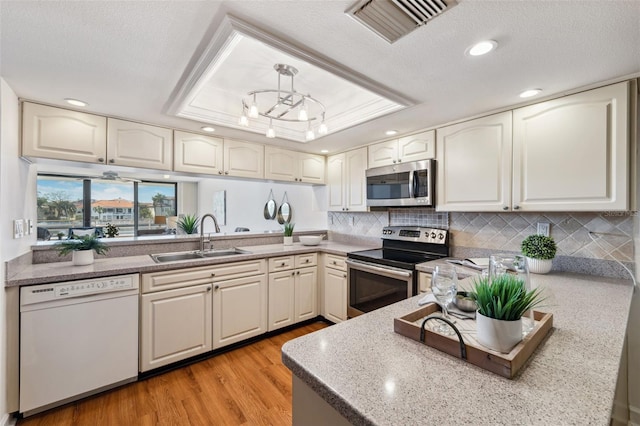 kitchen with a textured ceiling, stainless steel appliances, sink, light hardwood / wood-style flooring, and hanging light fixtures