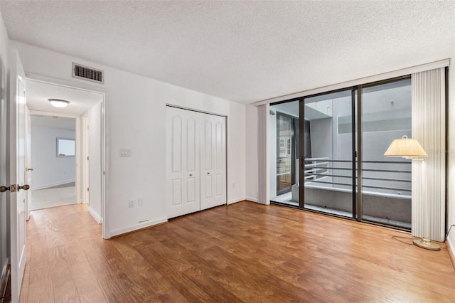 unfurnished bedroom with access to exterior, a textured ceiling, hardwood / wood-style flooring, and a closet