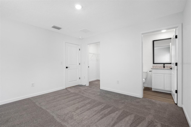 unfurnished bedroom featuring dark colored carpet, ensuite bath, a textured ceiling, a closet, and a spacious closet