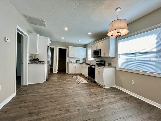 kitchen featuring appliances with stainless steel finishes, hanging light fixtures, sink, white cabinets, and dark wood-type flooring