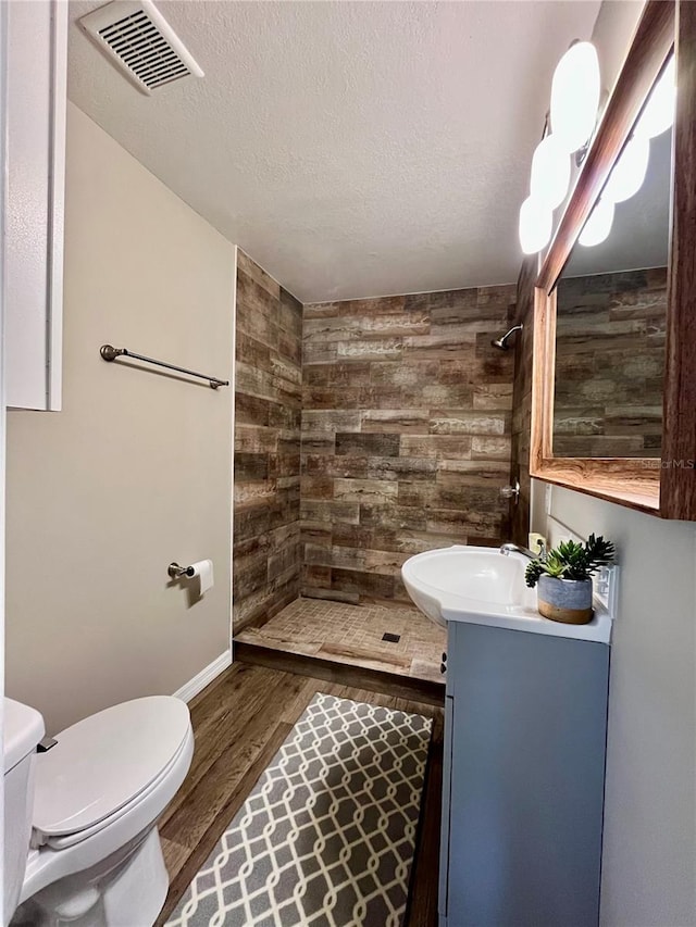 bathroom with wood-type flooring, toilet, a textured ceiling, wooden walls, and vanity