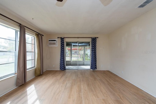 empty room with a wall unit AC, ceiling fan, plenty of natural light, and light hardwood / wood-style flooring