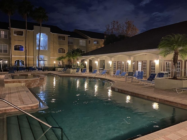 pool at twilight featuring a patio and a hot tub