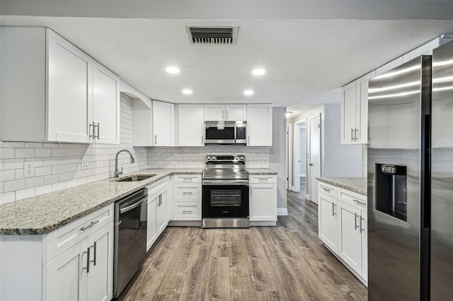 kitchen featuring stainless steel appliances, hardwood / wood-style flooring, sink, light stone countertops, and white cabinetry