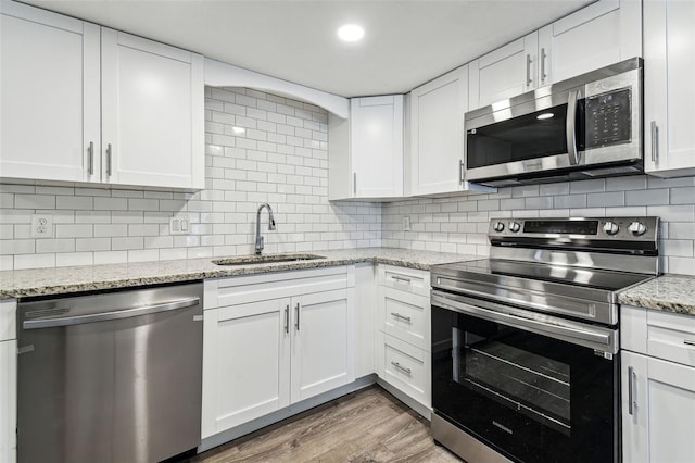 kitchen featuring sink, appliances with stainless steel finishes, hardwood / wood-style floors, white cabinets, and decorative backsplash