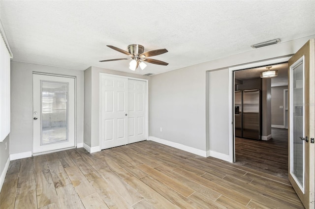 unfurnished bedroom featuring a textured ceiling, wood-type flooring, ceiling fan, and stainless steel fridge