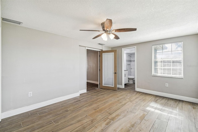 unfurnished bedroom with light hardwood / wood-style floors, a textured ceiling, ensuite bathroom, ceiling fan, and a closet