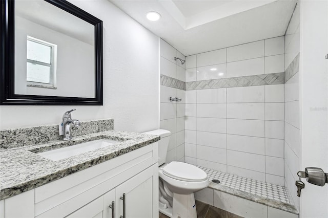 bathroom with wood-type flooring, vanity, toilet, and tiled shower