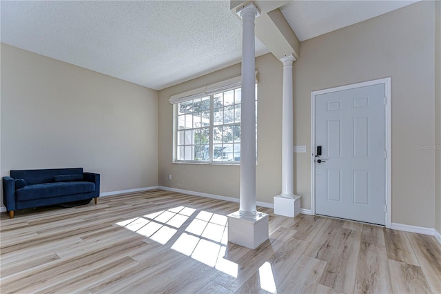 entrance foyer with light wood-type flooring, a textured ceiling, and decorative columns