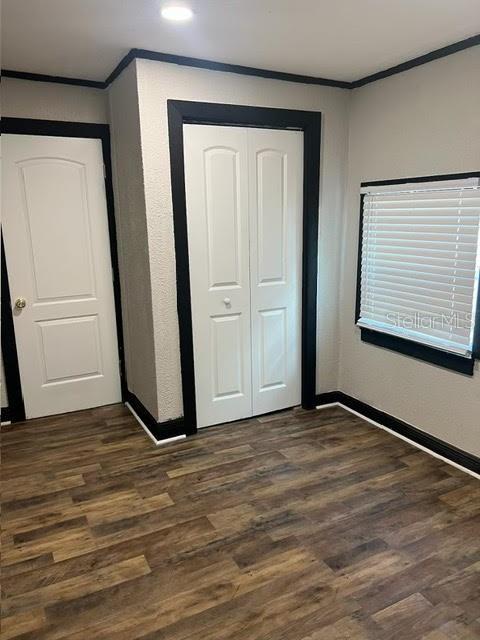 unfurnished bedroom with dark wood-type flooring, a closet, and crown molding