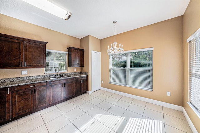 kitchen with sink, dark stone countertops, light tile patterned floors, dark brown cabinets, and a notable chandelier