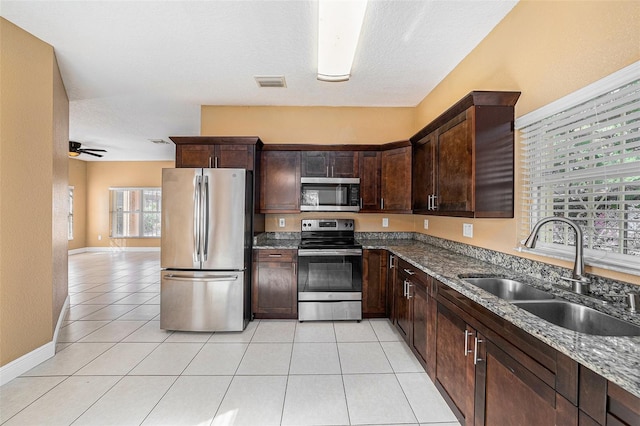 kitchen featuring dark stone counters, appliances with stainless steel finishes, light tile patterned floors, sink, and ceiling fan