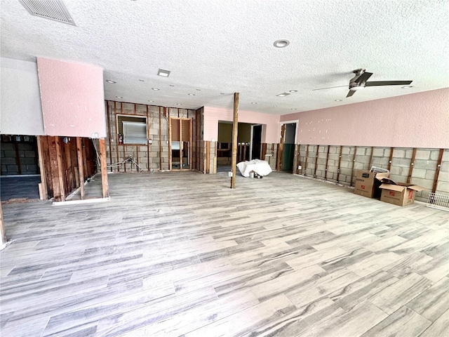 basement featuring light hardwood / wood-style floors, ceiling fan, and a textured ceiling