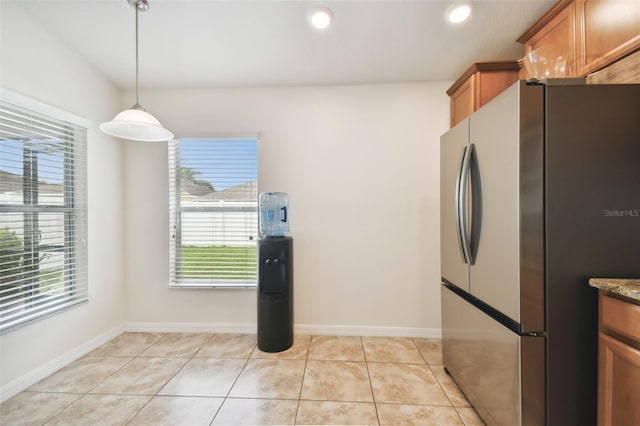 kitchen with light tile patterned floors, decorative light fixtures, stone counters, and stainless steel fridge