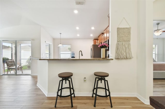 kitchen with pendant lighting, stainless steel fridge, a kitchen breakfast bar, and light hardwood / wood-style flooring