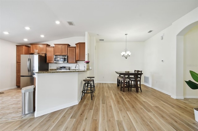 kitchen with light wood-type flooring, appliances with stainless steel finishes, kitchen peninsula, and dark stone counters