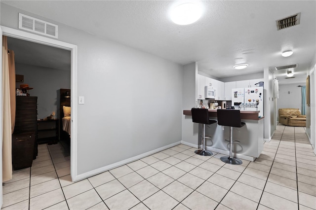 kitchen featuring a textured ceiling, light tile patterned floors, a kitchen breakfast bar, white cabinetry, and white appliances