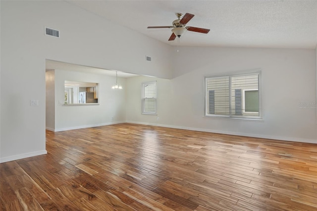 spare room with a textured ceiling, ceiling fan with notable chandelier, hardwood / wood-style flooring, and high vaulted ceiling