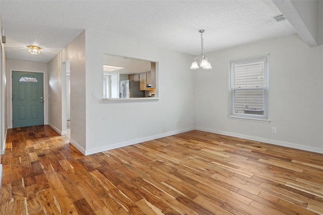 unfurnished dining area featuring a chandelier, a textured ceiling, and hardwood / wood-style flooring