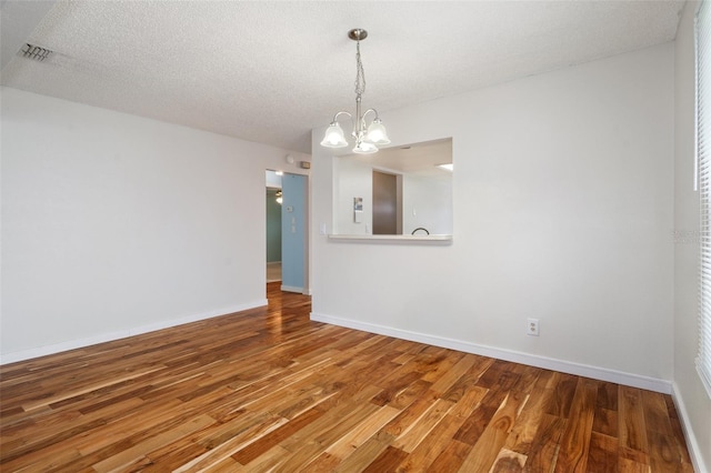 empty room featuring wood-type flooring, a textured ceiling, and an inviting chandelier