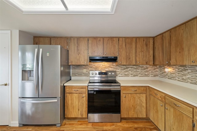 kitchen with appliances with stainless steel finishes, light wood-type flooring, and backsplash