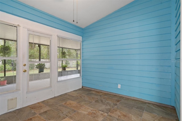 doorway to outside with a healthy amount of sunlight, lofted ceiling, and wooden walls