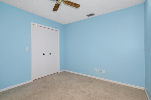 unfurnished bedroom featuring a textured ceiling, a closet, ceiling fan, and light colored carpet