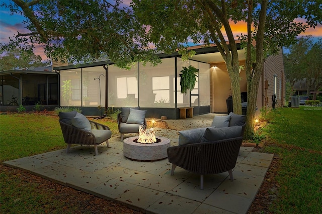 patio terrace at dusk with a lawn, a sunroom, and an outdoor fire pit