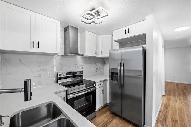 kitchen with light hardwood / wood-style flooring, wall chimney range hood, white cabinets, and stainless steel appliances