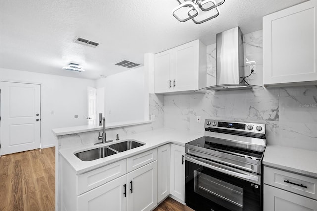 kitchen with stainless steel electric range, white cabinets, sink, and wall chimney range hood